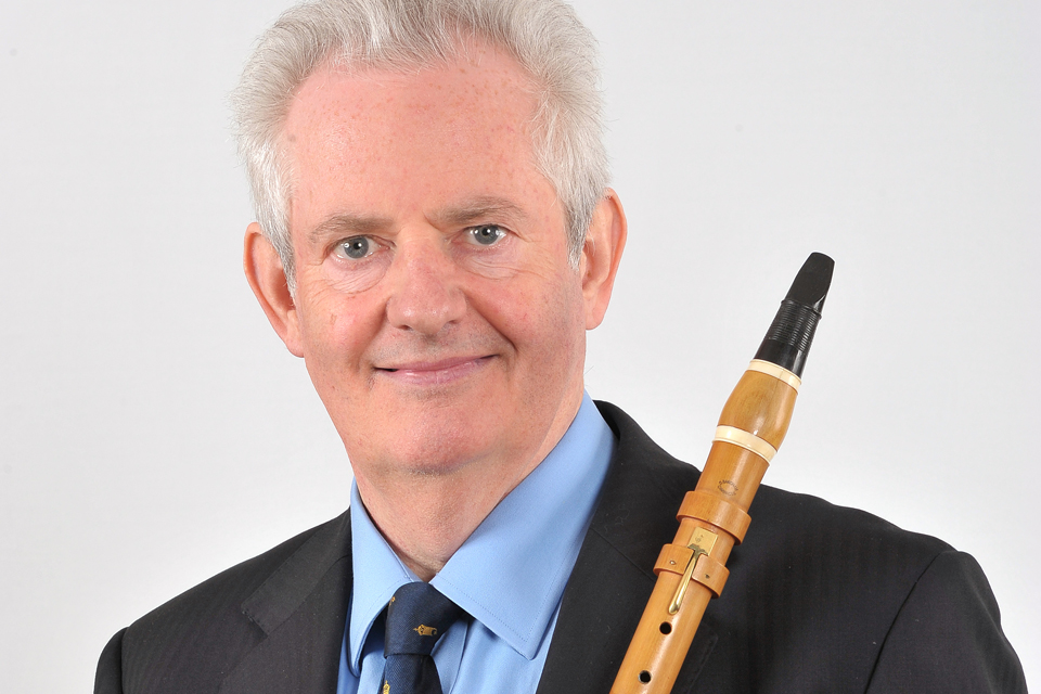 A white man, smiling at the camera, wearing a suit and holding a clarinet.